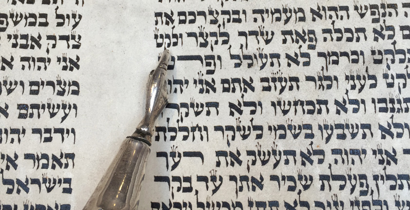 A silver yad pointer resting on a handwritten Torah scroll open to Leviticus